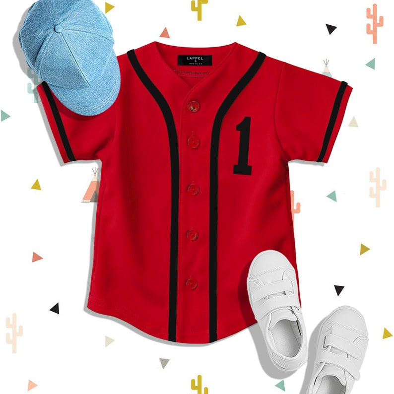 Op de afbeelding: Rood baseballshirt met zwarte bies en het nummer "1" op de voorkant. Het shirt heeft een knoopsluiting aan de voorkant en korte mouwen. Een blauwe baseballpet en witte sneakers zijn ook afgebeeld.