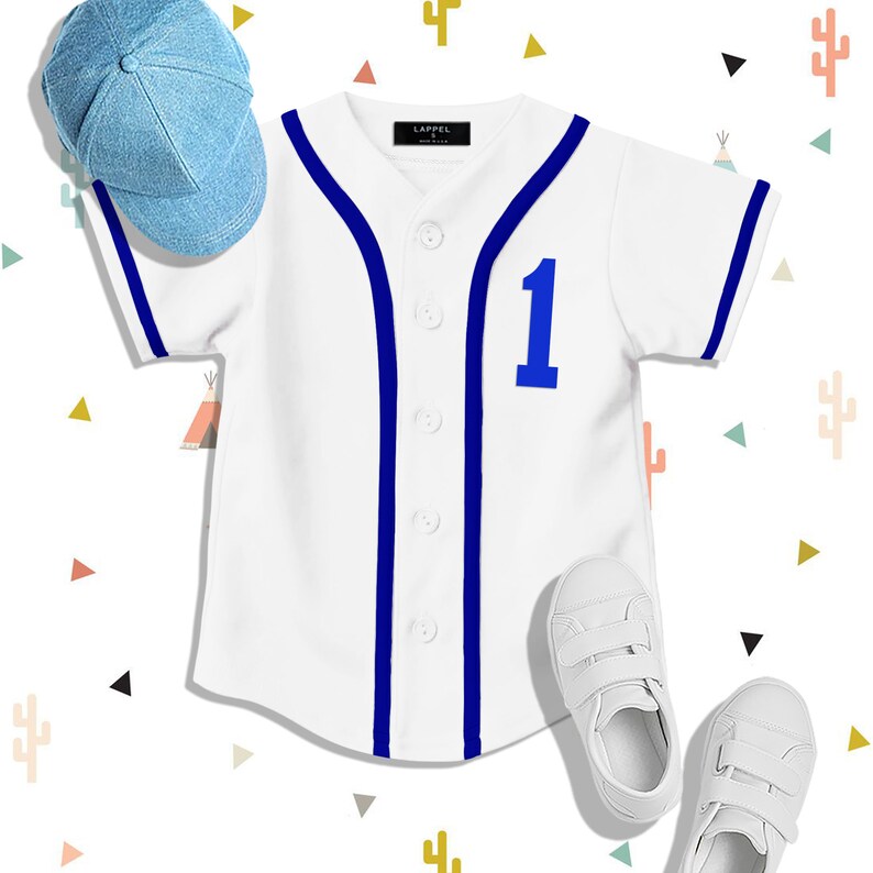 Op de afbeelding: Een wit baseballshirt met blauwe bies en het nummer 1 op de voorkant. Het shirt wordt gecombineerd met een lichtblauwe baseballpet en witte sneakers.