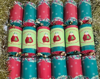 May include: A set of 12 Christmas crackers with a green and red design. Each cracker features a cartoon cat wearing a Christmas sweater and the text "Robbie & Alexander's Cracking Kitty Crackers".