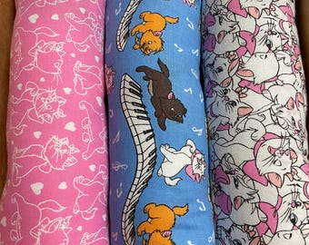 May include: Three rectangular cat-themed pillows. One is pink with white cat outlines and hearts. Another is blue with cat illustrations, musical notes, and a piano. The third is white with pink cat outlines.