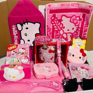 May include: A collection of pink Hello Kitty themed items, including a wallet, comb, sunglasses, pen, notebook, and a Hello Kitty Uno card game. The items are arranged in a box.