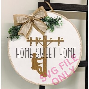 Può includere: Cartello rotondo in legno con la scritta "HOME SWEET HOME" e la silhouette di un elettricista su un palo della luce. Decorato con un fiocco di juta e verde, con una corda per appenderlo. Tema casa.