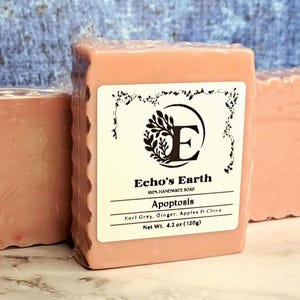 May include: Three rectangular bars of light pink soap wrapped in clear plastic. The center bar features a white label with the text Echo's Earth, 100% Handmade Soap, Apoptosis, Earl Grey, Ginger, Apples & Clove, and Net Wt. 4.2 oz (120g).