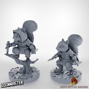 May include: Two grey 3D-printed figurines of anthropomorphic squirrels in hooded cloaks, holding daggers. One squirrel stands on a tree branch, the other on a circular base. The text "GOONMASTER" and "LITTLE RED'S 3D EMPORIUM" are visible.