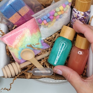 May include: A gift box filled with bath and body products. The box contains bath bombs, bath salts, bath fizzies, and bath oils. The products are all in different colors and have a variety of scents.