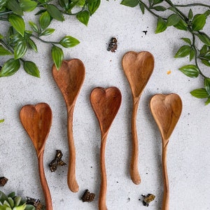 May include: Five wooden spoons with heart-shaped bowls. The spoons are made of natural wood and have a light brown color. They are arranged on a white surface.