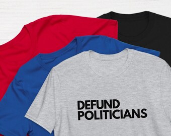 Peut inclure: Quatre t-shirts empilés les uns sur les autres. Le t-shirt du dessus est gris avec le texte "DEFUND POLITICIANS" imprimé en noir. Les autres t-shirts sont rouge, bleu et noir.