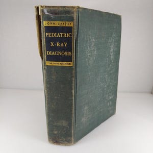 May include: A vintage medical textbook titled "Pediatric X-Ray Diagnosis" by John Caffey. The book has a dark teal cover with gold lettering and a gold label. The book is from Year Book Publishers.