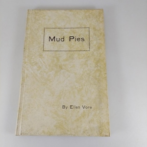 May include: A vintage book titled "Mud Pies" by Ellen Vore. The cover is a light beige with a textured pattern. The title is in a rectangular dotted frame. The author's name is printed below the title.