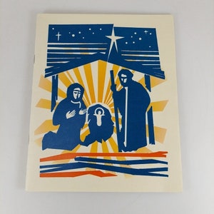 Op de afbeelding: Een blauwe en gele kerstkaart met een kerststal. De kaart toont een ster, een kribbe en drie figuren: Maria, Jozef en het kindje Jezus.