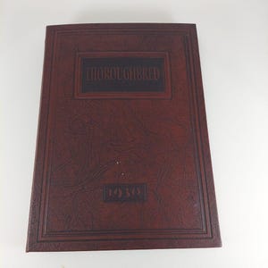 Könnte beinhalten: Ein dunkelbraunes, ledergebundenes Buch mit dem Titel "Thoroughbred" und dem Jahr "1930" auf dem Einband geprägt.