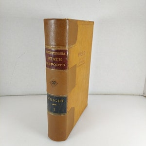 Op de afbeelding: Een vintage boek getiteld "Pennsylvania State Reports" met een bruine leren rug en een tan cover. De rug heeft de titel in gouden letters op een bordeauxrode achtergrond, met het nummer "37" in een ruitvorm. Het boek is gelabeld "Wright 1".