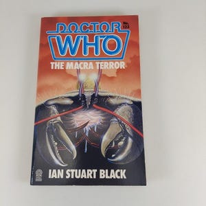 May include: A vintage paperback book titled "Doctor Who: The Macra Terror" by Ian Stuart Black. The cover features a menacing crab-like creature in dark blue and black against an orange and red background. The book is a Target edition.