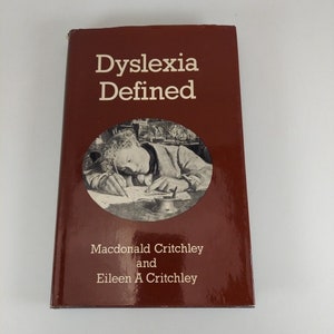 May include: A red hardcover book titled "Dyslexia Defined" by Macdonald Critchley and Eileen A Critchley. The cover features a black and white illustration of a person writing at a desk.