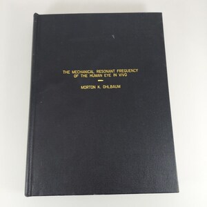 May include: Black hardback book with gold lettering on the spine. The title is "The Mechanical Resonant Frequency of the Human Eye in Vivo" by Morton K. Ohlbaum.