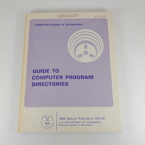Op de afbeelding: Een paarse omslag van een gids voor computerprogramma-directories, uitgegeven door het National Bureau of Standards, U.S. Department of Commerce. De omslag toont een gestileerde afbeelding van een computerbandrol.