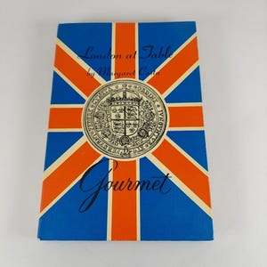 May include: A book titled "London at Table" by Margaret Costa, with a cover design featuring the Union Jack flag in blue, red, and white. The cover also includes a central emblem and the word "Gourmet".