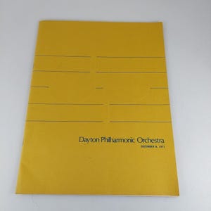 Puede incluir: Un programa amarillo de la Orquesta Filarmónica de Dayton, con líneas horizontales y el nombre de la orquesta. La fecha "DECEMBER 8, 1971" está impresa debajo.