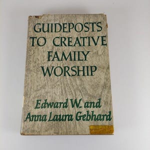 Może przedstawiać: Antyczna książka zatytułowana "Guideposts to Creative Family Worship" autorstwa Edwarda W. i Anny Laury Gebhard. Okładka książki jest jasnobrązowa z zielonym tekstem.