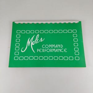 Puede incluir: Una tarjeta verde con texto blanco que dice "Moles COMMAND PERFORMANCE". La tarjeta tiene un borde blanco de pequeños rectángulos alrededor de los bordes.