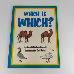 Puede incluir: Un libro infantil vintage titulado "Which is Which?" presenta ilustraciones de camellos, un ganso y un pato. La portada tiene un borde azul, amarillo y verde, con el título en letras azules grandes.