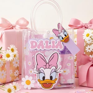 Peut inclure: Un sac fourre-tout en plastique transparent avec un motif de marguerites roses et blanches, un grand graphique de Daisy Duck et le nom DALIA en lettres roses. Le sac possède des poignées transparentes, une fermeture à pression et une étiquette.