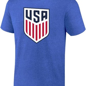 May include: A royal blue t-shirt with a white and red USA crest graphic. The crest features a shield with the letters USA and red and white stripes.