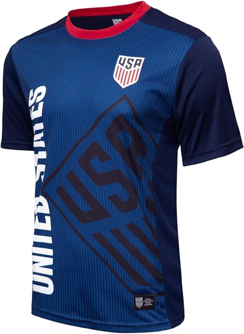 May include: A navy blue soccer jersey with a white "UNITED STATES" graphic on the left side and a red, white, and blue "USA" logo on the right side. The jersey has a red collar and a white stripe pattern.