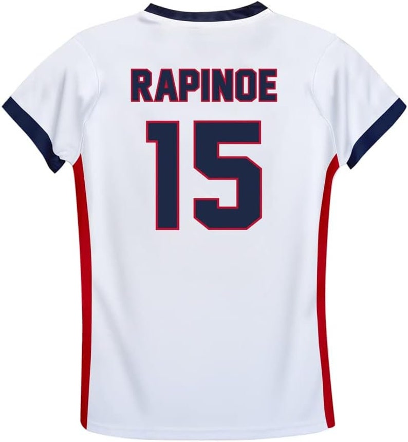 May include: White soccer jersey with red and blue trim. The back of the jersey has the name "RAPINOE" and the number "15" printed in blue with a red outline.