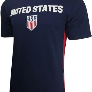 May include: A navy blue football shirt with red and white trim. The shirt has the words "UNITED STATES" printed on the front, along with a shield with the letters "USA" inside.
