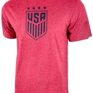 May include: Red short-sleeved t-shirt with a blue and white USA crest graphic. The crest features five stars above the word "USA" and vertical stripes.