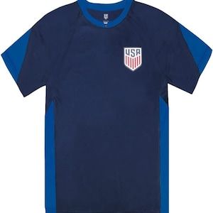 May include: A navy blue short-sleeved t-shirt with blue side panels. The shirt has a white crew neck and a small embroidered USA crest on the front.