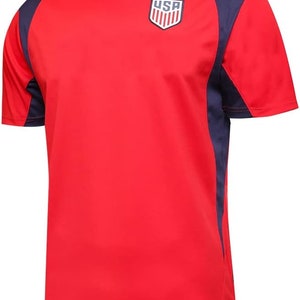 May include: Red short-sleeved t-shirt with navy blue accents on the sleeves and shoulders. The shirt features a white and blue USA logo on the chest.