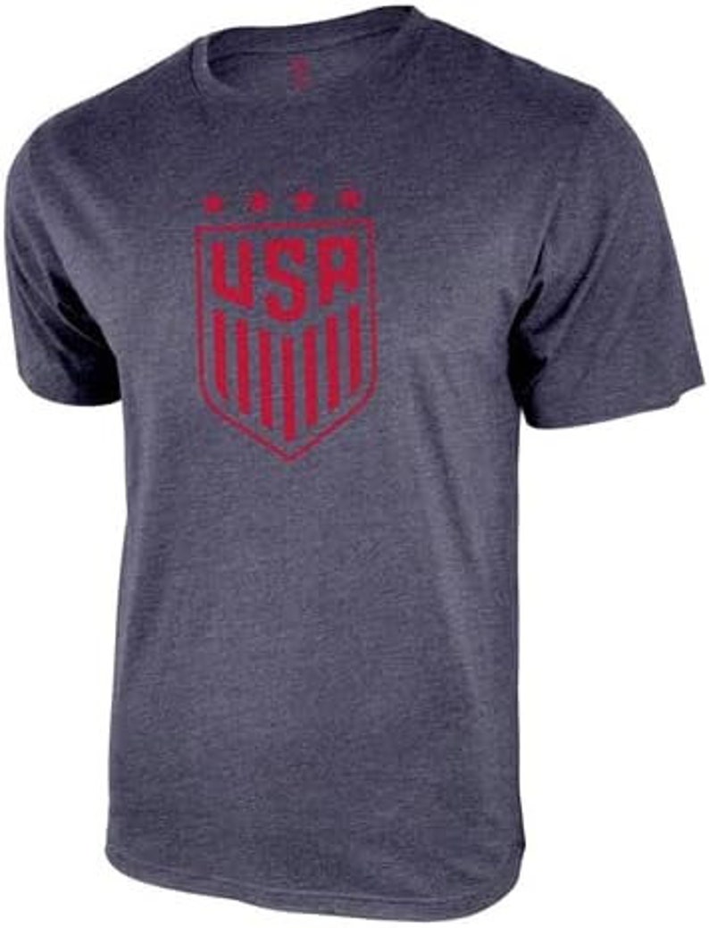 May include: A navy blue t-shirt with a red USA crest graphic. The crest features a shield with vertical stripes and the letters USA in a bold font.