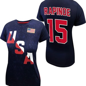 May include: A navy blue t-shirt with the text "USA" printed in red, white, and blue on the front and the text "RAPINOE 15" printed in red on the back.