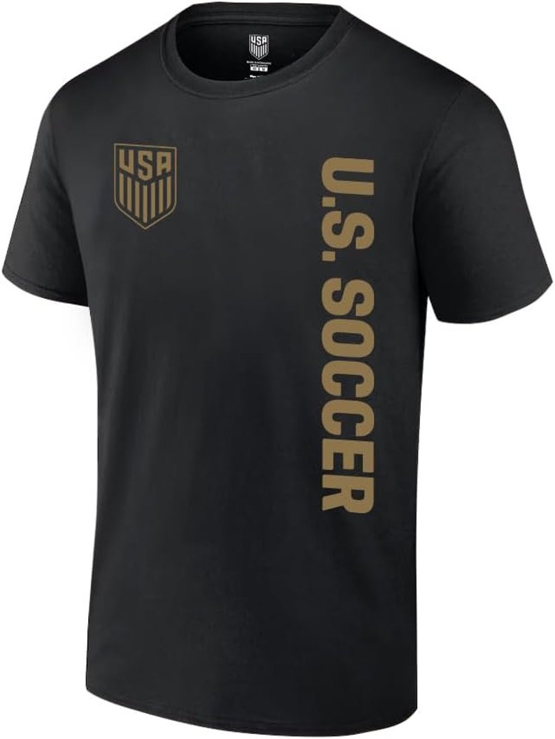 K&ouml;nnte beinhalten: Schwarzes T-Shirt mit einem goldenen U.S. Soccer-Logo auf der linken Brust und "U.S. SOCCER" vertikal auf der rechten Seite gedruckt.