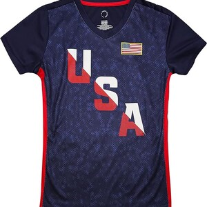 Pu&ograve; includere: Una maglietta blu navy con una grafica USA in rosso, bianco e blu e una piccola bandiera americana sul petto. La maglietta ha pannelli laterali rossi e un collo a V.