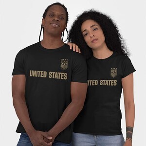 May include: Two black t-shirts with a gold shield and stars graphic and the text "UNITED STATES".