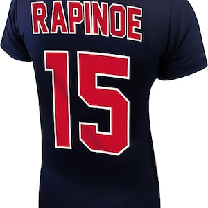 May include: A navy blue jersey with the name "RAPINOE" and the number "15" printed on the back in red with white outlines.