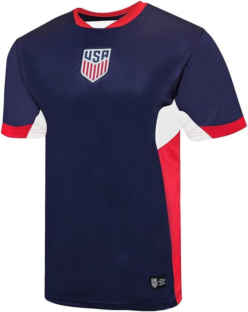 K&ouml;nnte beinhalten: Ein marineblaues Fu&szlig;balltrikot mit wei&szlig;en und roten Akzenten. Das Trikot tr&auml;gt das USA-Logo auf der Vorderseite.