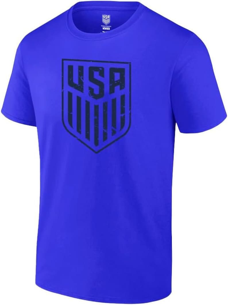 May include: A royal blue t-shirt featuring a distressed navy blue graphic of the USA shield logo.