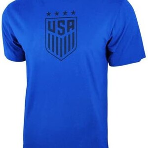 May include: A royal blue t-shirt with a navy blue USA crest featuring five stars and the word "USA" in a shield shape.