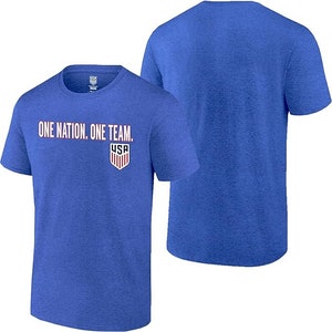 May include: A royal blue t-shirt with the words "One Nation. One Team." printed in white and red on the front. A small USA logo is printed below the text. The back of the shirt is plain.