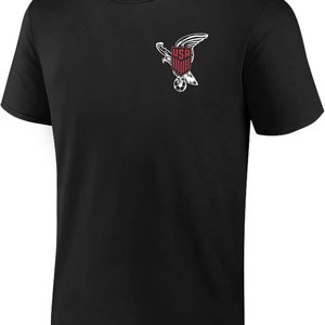 May include: Black t-shirt with a white graphic of an eagle holding a soccer ball. The eagle is holding a shield with the word "USA" on it.