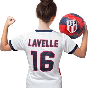 May include: White soccer jersey with blue trim and the name "LAVELLE" and number "16" on the back. A person is wearing the jersey and holding a red, white, and blue soccer ball with the word "USA" on it.