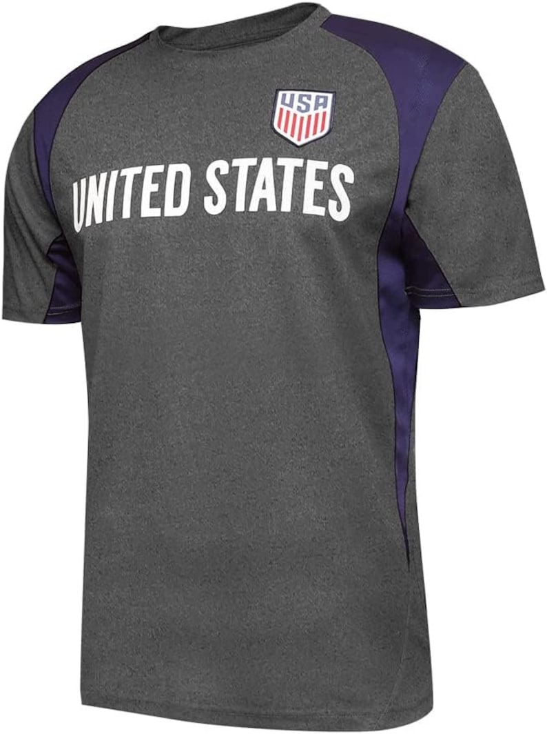 May include: A heather grey t-shirt with purple accents on the sleeves. The shirt has a white graphic of the United States flag and the text "UNITED STATES".