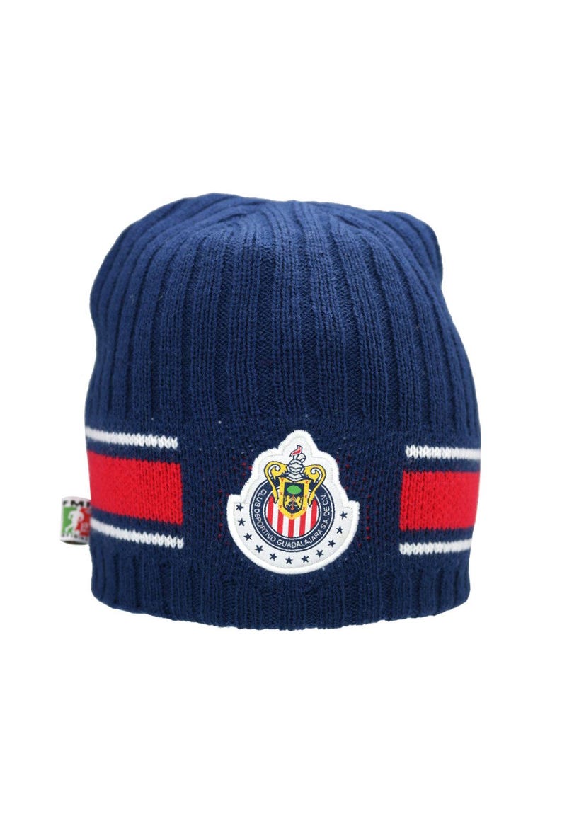 May include: A blue knitted beanie with a red and white stripe pattern. The beanie features a white embroidered logo with the text "Club Deportivo Guadalajara S.A." and a crest.