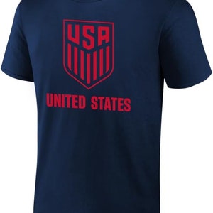 Puede incluir: Una camiseta azul marino con un logotipo de EE. UU. rojo y las palabras "UNITED STATES" impresas en la parte delantera.