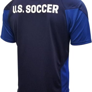 May include: A navy blue soccer jersey with royal blue accents on the sleeves and sides. The back of the jersey has "U.S. SOCCER" printed in white.