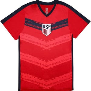 May include: Red V-neck t-shirt with navy blue accents on the sleeves and shoulders. The shirt features a navy blue horizontal stripe across the chest and a USA emblem. The shirt has a textured design.